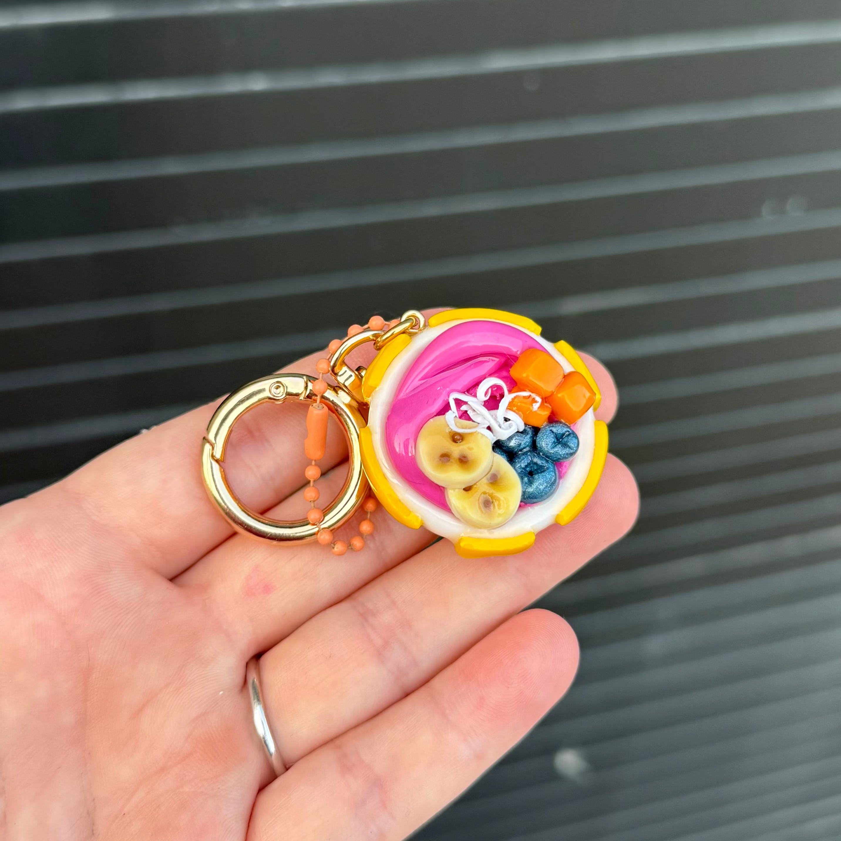 Polymer clay keychain that features an Açaí smoothie in a white bowl with yellow stars. Mango chunks, blueberries, banana slices, and coconut shavings are toppings in the bowl. 