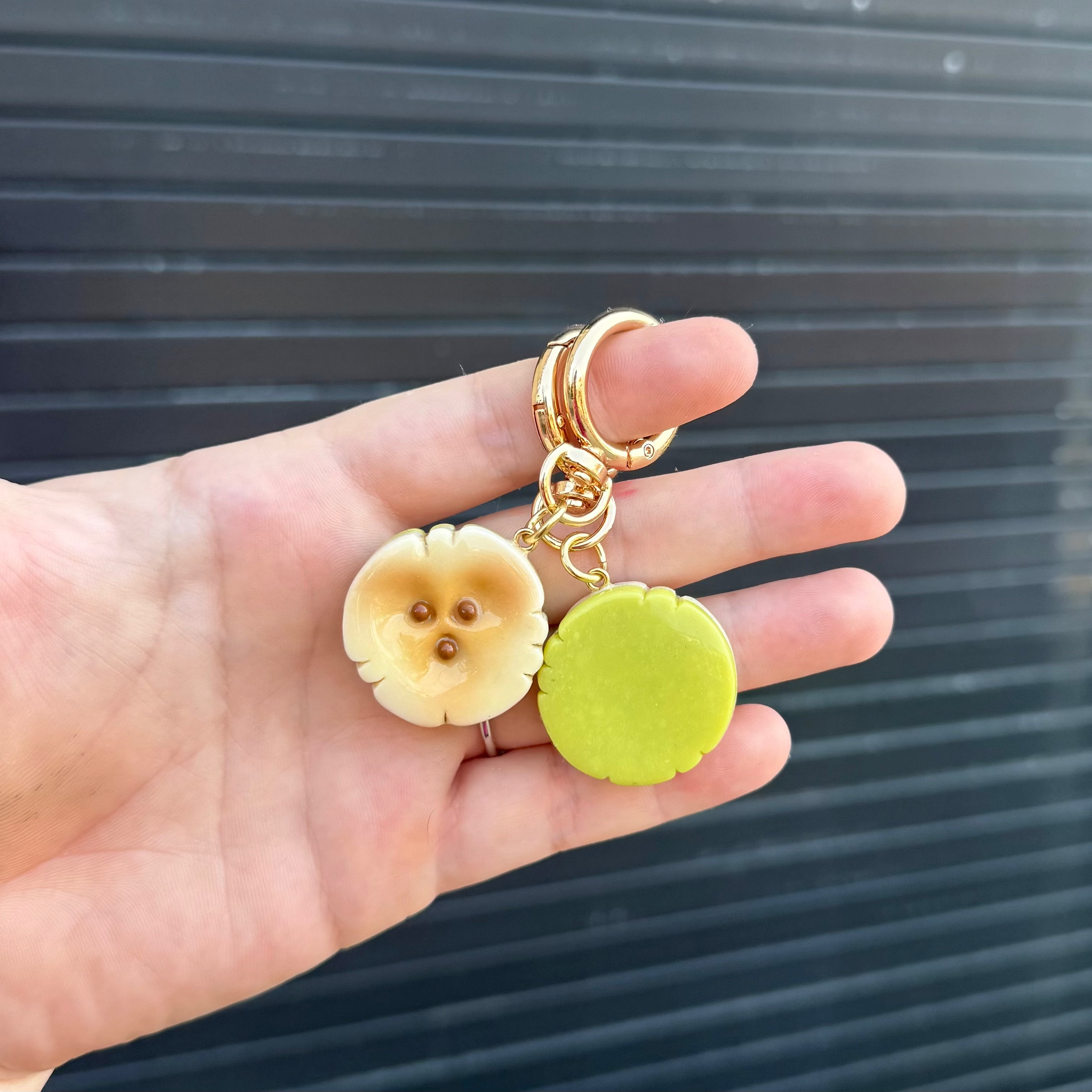 a hand holding two banana slice keychains. one facing forward and the other showing the green backside. 