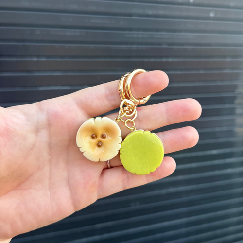 a hand holding two banana slice keychains. one facing forward and the other showing the green backside. 