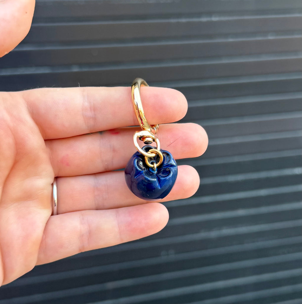 polymer clay blueberry charm hanging from keychain against a graphite colored wall. 