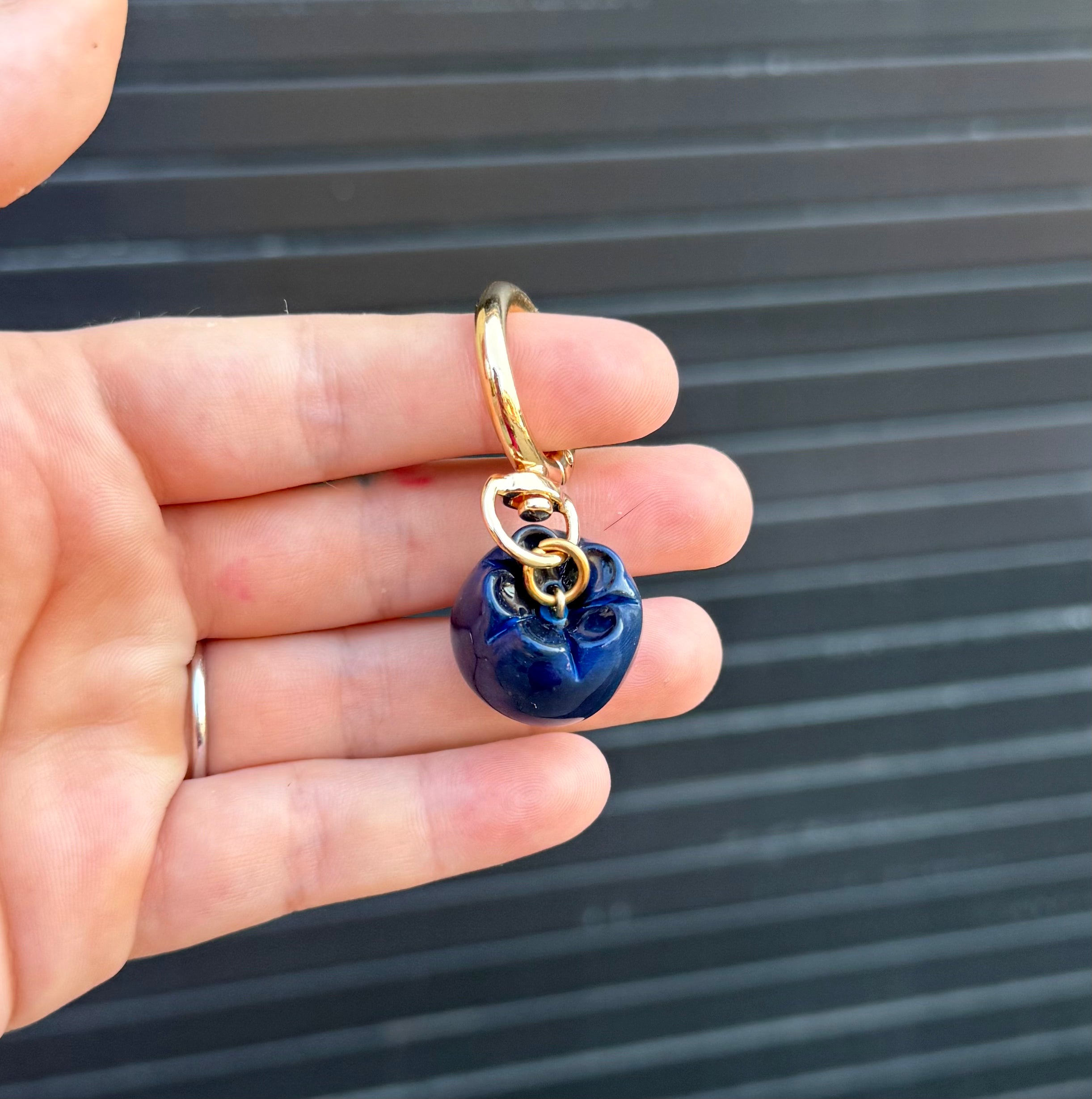 polymer clay blueberry charm hanging from keychain against a graphite colored wall. 
