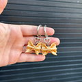 two shimmery gold polymer clay charms shaped like farfalle pasta. 