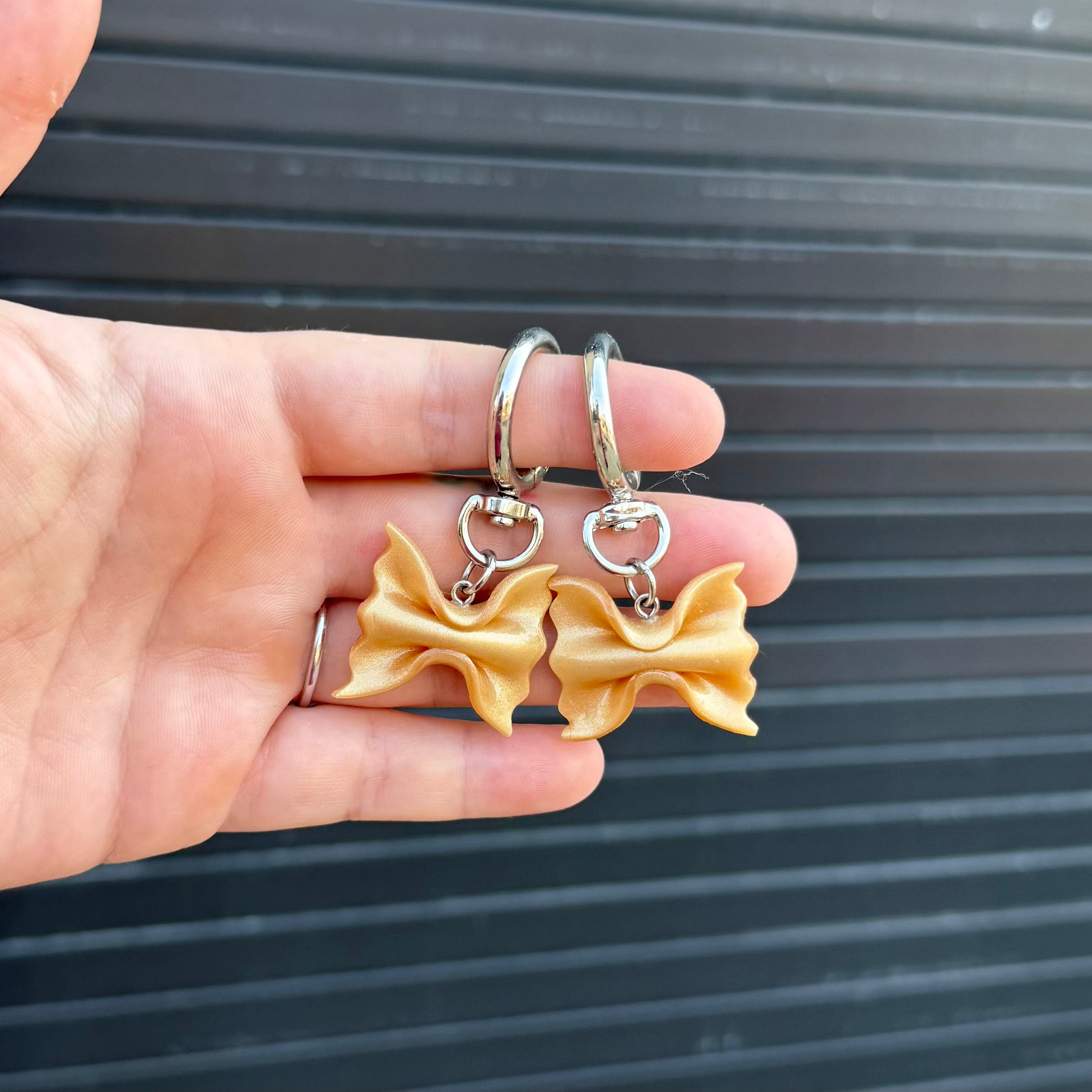 two shimmery gold polymer clay charms shaped like farfalle pasta. 