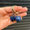 a hand holding two blueberry dangle keychains in front of a graphite back drop. 