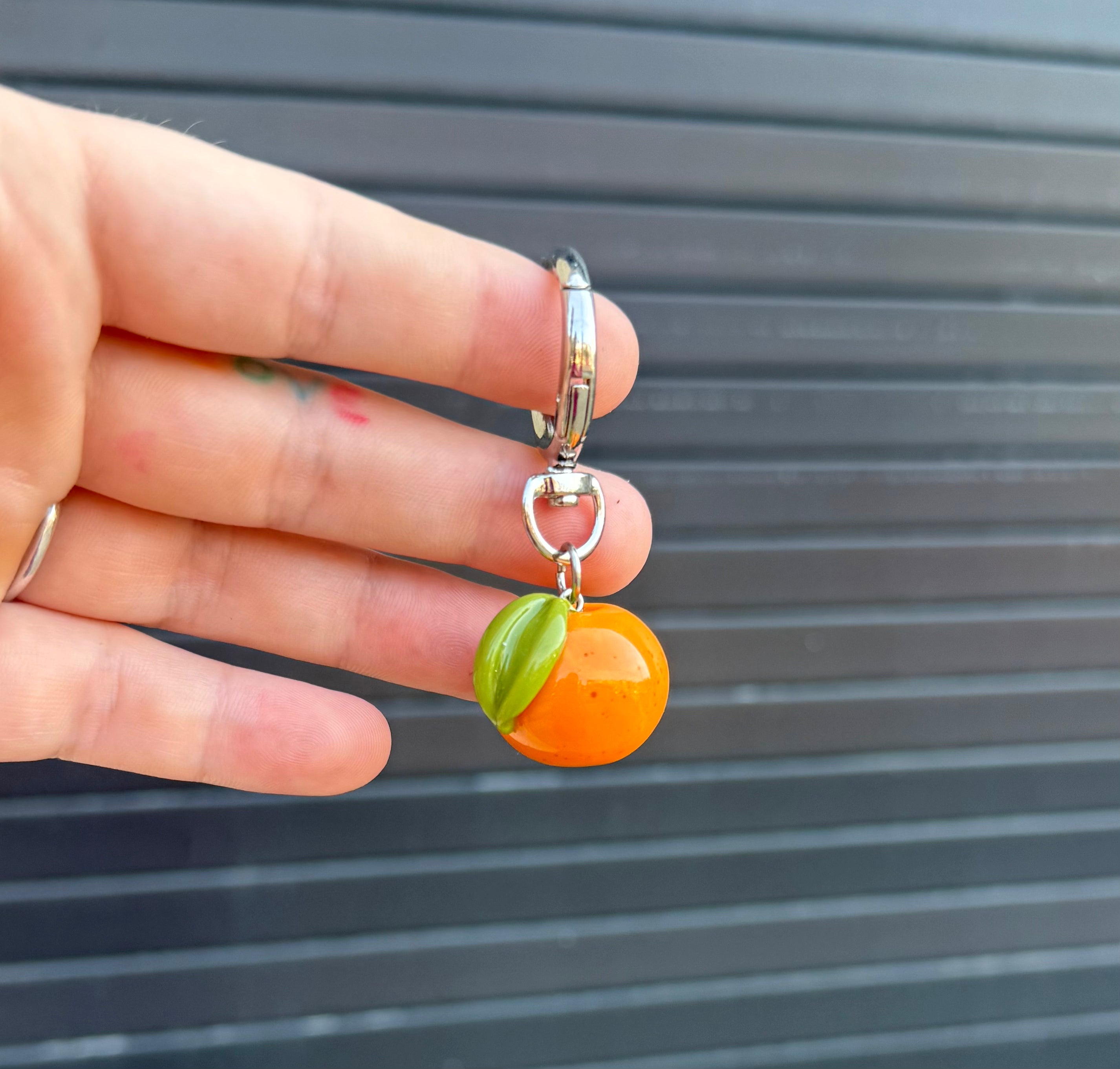 polymer clay orange fruit charm on a keychain being held against a graphite colored background. 