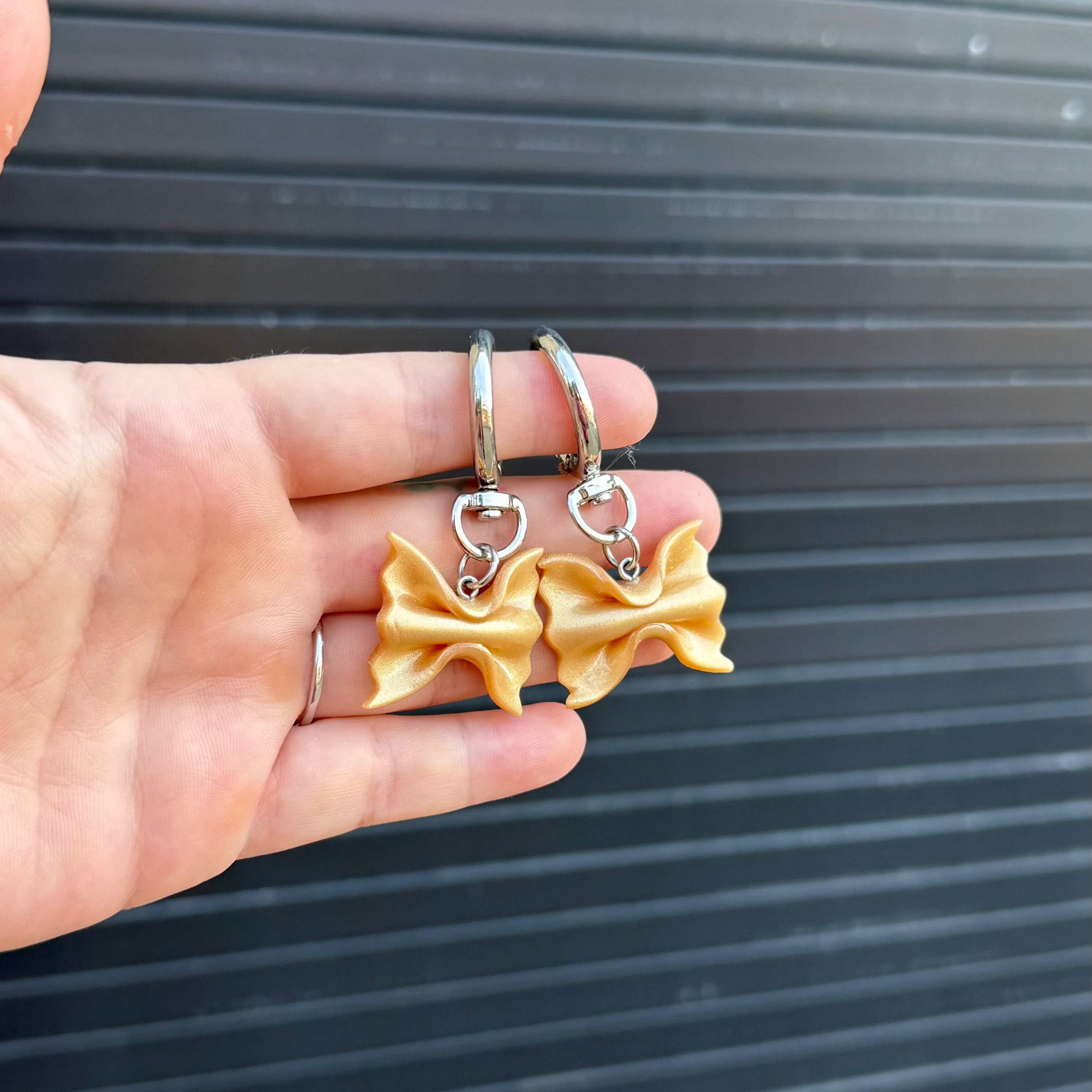 bowtie pasta keychains held up in front of a graphite colored background. 