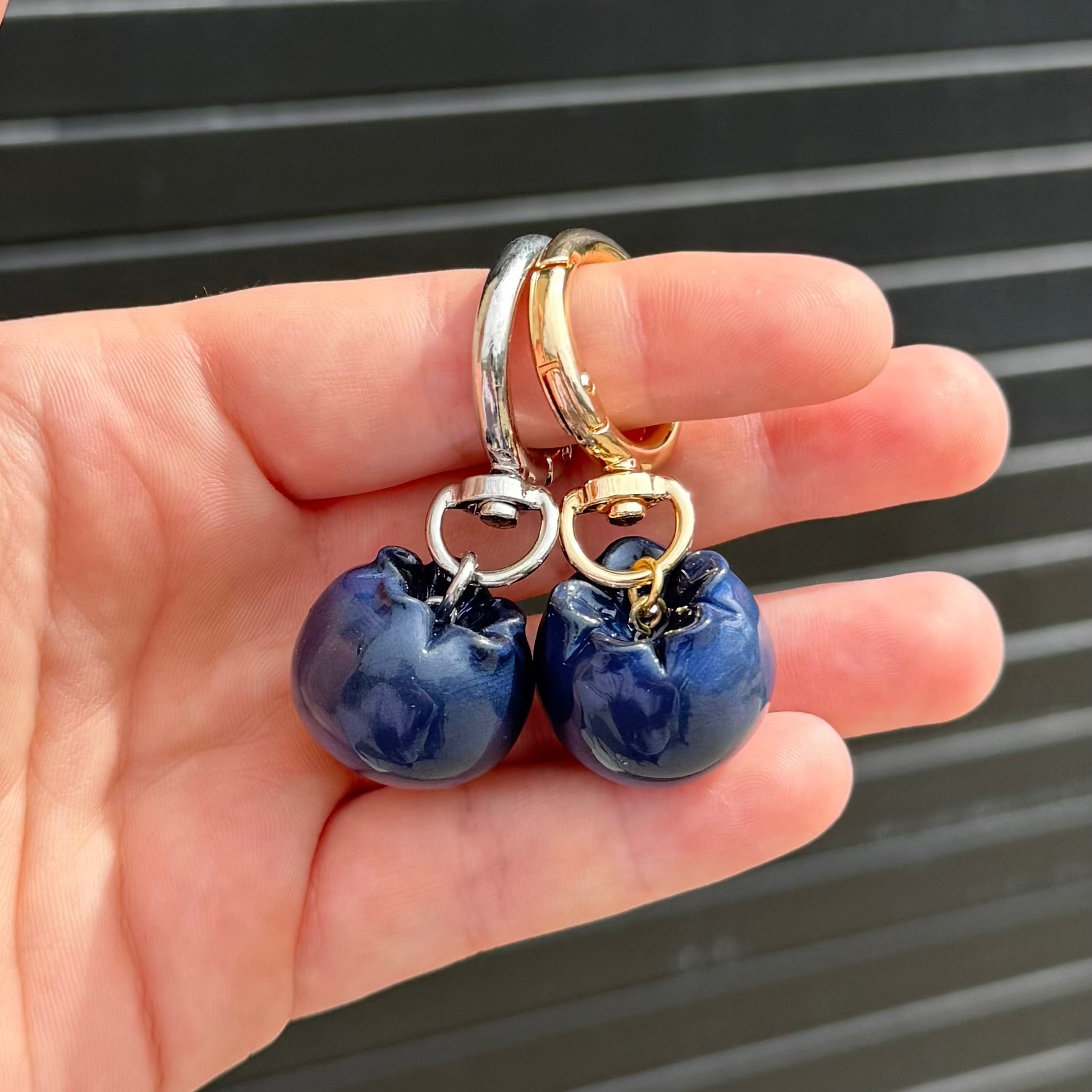 two blueberry charms hanging from keychains against a graphite colored wall. 
